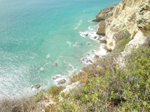 Blick von einer Steilküste auf türkisblaues Wasser.