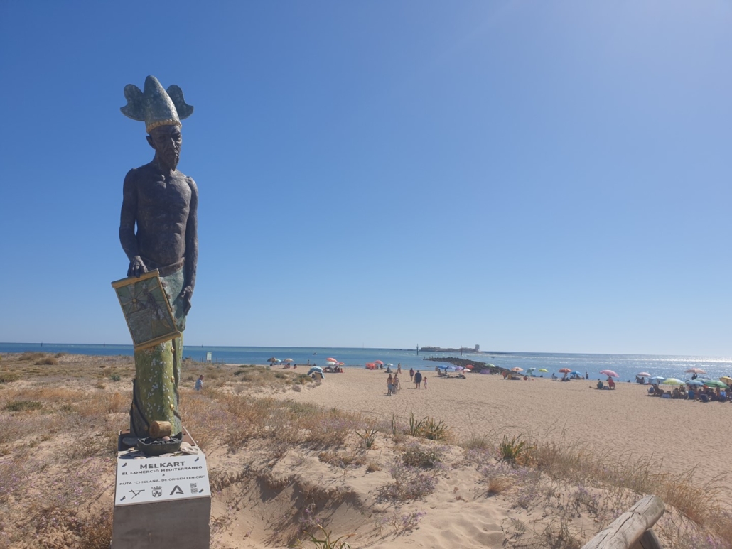 Playa de Sancti Petri in Chiclana de la Frontera mit Melkart-Statue und dem Eiland von Sancti Petri im Hintergrund.